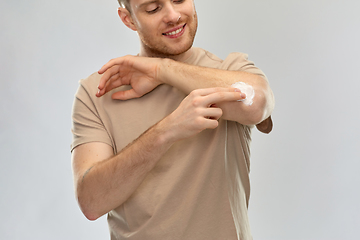 Image showing young man applying pain medication to his elbow