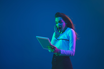 Image showing Caucasian woman\'s portrait isolated on blue studio background in pink-green neon light, stylish and beautiful