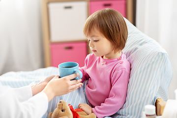 Image showing doctor giving hot tea to sick little girl in bed