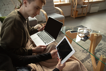 Image showing Attractive young couple using devices together, tablet, laptop, smartphone, headphones wireless. Gadgets and technologies connecting people all around the world