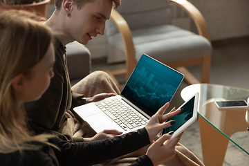 Image showing Attractive young couple using devices together, tablet, laptop, smartphone, headphones wireless. Gadgets and technologies connecting people all around the world