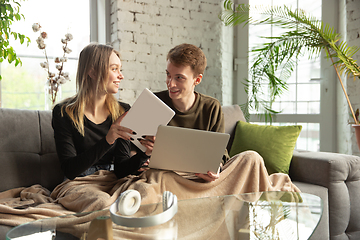 Image showing Attractive young couple using devices together, tablet, laptop, smartphone, headphones wireless. Gadgets and technologies connecting people all around the world