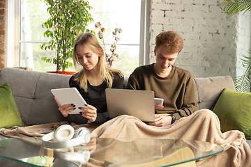 Image showing Attractive young couple using devices together, tablet, laptop, smartphone, headphones wireless. Gadgets and technologies connecting people all around the world