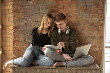 Image showing Attractive young couple using devices together, tablet, laptop, smartphone, headphones wireless. Gadgets and technologies connecting people all around the world