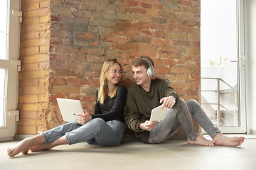 Image showing Attractive young couple using devices together, tablet, laptop, smartphone, headphones wireless. Gadgets and technologies connecting people all around the world