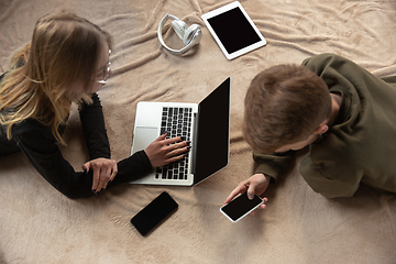 Image showing Attractive young couple using devices together, tablet, laptop, smartphone, headphones wireless. Gadgets and technologies connecting people all around the world