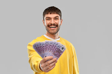 Image showing smiling young man in yellow sweatshirt with money