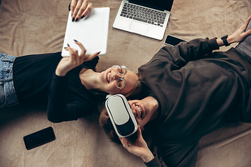 Image showing Attractive young couple using devices together, tablet, laptop, smartphone, headphones wireless. Gadgets and technologies connecting people all around the world