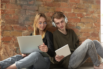 Image showing Attractive young couple using devices together, tablet, laptop, smartphone, headphones wireless. Gadgets and technologies connecting people all around the world