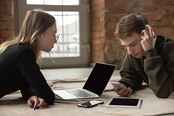 Image showing Attractive young couple using devices together, tablet, laptop, smartphone, headphones wireless. Gadgets and technologies connecting people all around the world