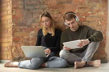 Image showing Attractive young couple using devices together, tablet, laptop, smartphone, headphones wireless. Gadgets and technologies connecting people all around the world