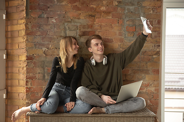 Image showing Attractive young couple using devices together, tablet, laptop, smartphone, headphones wireless. Gadgets and technologies connecting people all around the world