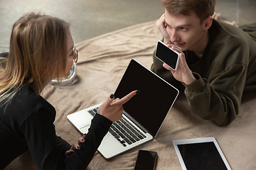 Image showing Attractive young couple using devices together, tablet, laptop, smartphone, headphones wireless. Gadgets and technologies connecting people all around the world