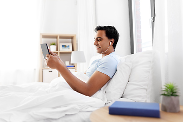 Image showing happy indian man with tablet pc in bed at home