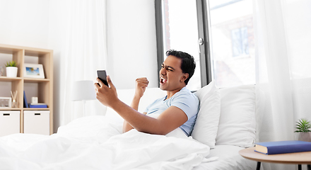 Image showing happy indian man with smartphone in bed at home