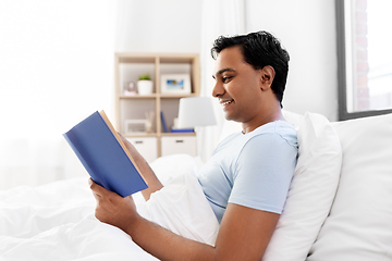 Image showing happy indian man reading book in bed at home