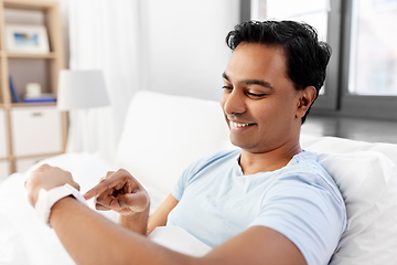 Image showing happy indian man with smart watch in bed at home