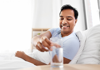 Image showing happy indian man drinking water lying in bed