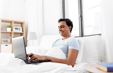 Image showing happy indian man with laptop in bed at home