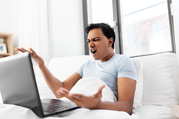 Image showing angry indian man with laptop in bed at home