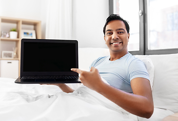 Image showing happy indian man showing his laptop in bed at home