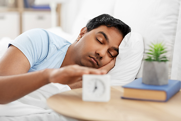 Image showing sleepy indian man with alarm clock lying in bed