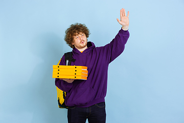 Image showing Contacless delivery service during quarantine. Man delivers food and shopping bags during insulation. Emotions of deliveryman isolated on blue background.