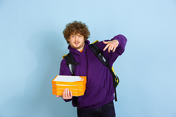 Image showing Contacless delivery service during quarantine. Man delivers food and shopping bags during insulation. Emotions of deliveryman isolated on blue background.