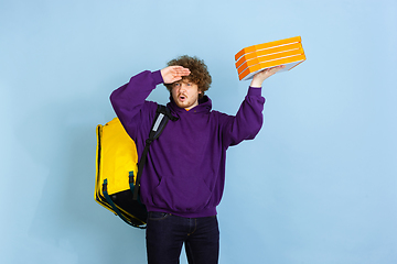 Image showing Contacless delivery service during quarantine. Man delivers food and shopping bags during insulation. Emotions of deliveryman isolated on blue background.