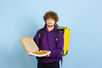 Image showing Contacless delivery service during quarantine. Man delivers food and shopping bags during insulation. Emotions of deliveryman isolated on blue background.