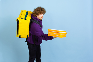 Image showing Contacless delivery service during quarantine. Man delivers food and shopping bags during insulation. Emotions of deliveryman isolated on blue background.