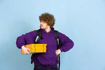 Image showing Contacless delivery service during quarantine. Man delivers food and shopping bags during insulation. Emotions of deliveryman isolated on blue background.