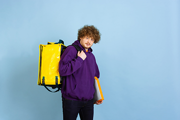 Image showing Contacless delivery service during quarantine. Man delivers food and shopping bags during insulation. Emotions of deliveryman isolated on blue background.