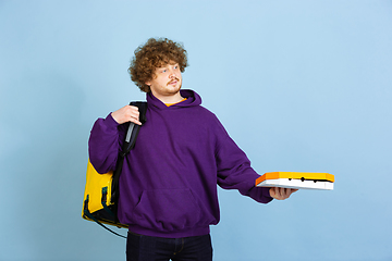 Image showing Contacless delivery service during quarantine. Man delivers food and shopping bags during insulation. Emotions of deliveryman isolated on blue background.