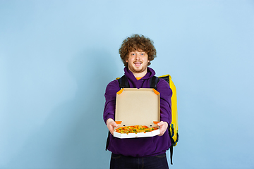 Image showing Contacless delivery service during quarantine. Man delivers food and shopping bags during insulation. Emotions of deliveryman isolated on blue background.