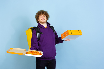 Image showing Contacless delivery service during quarantine. Man delivers food and shopping bags during insulation. Emotions of deliveryman isolated on blue background.