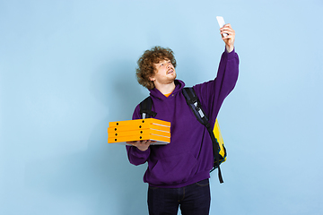 Image showing Contacless delivery service during quarantine. Man delivers food and shopping bags during insulation. Emotions of deliveryman isolated on blue background.