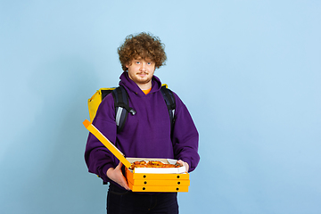 Image showing Contacless delivery service during quarantine. Man delivers food and shopping bags during insulation. Emotions of deliveryman isolated on blue background.