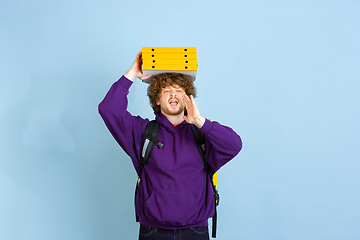 Image showing Contacless delivery service during quarantine. Man delivers food and shopping bags during insulation. Emotions of deliveryman isolated on blue background.