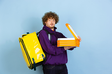 Image showing Contacless delivery service during quarantine. Man delivers food and shopping bags during insulation. Emotions of deliveryman isolated on blue background.