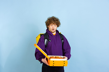 Image showing Contacless delivery service during quarantine. Man delivers food and shopping bags during insulation. Emotions of deliveryman isolated on blue background.