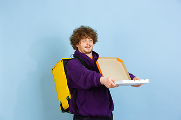 Image showing Contacless delivery service during quarantine. Man delivers food and shopping bags during insulation. Emotions of deliveryman isolated on blue background.