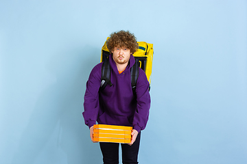 Image showing Contacless delivery service during quarantine. Man delivers food and shopping bags during insulation. Emotions of deliveryman isolated on blue background.