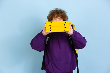 Image showing Contacless delivery service during quarantine. Man delivers food and shopping bags during insulation. Emotions of deliveryman isolated on blue background.