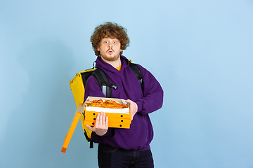 Image showing Contacless delivery service during quarantine. Man delivers food and shopping bags during insulation. Emotions of deliveryman isolated on blue background.