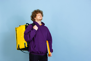 Image showing Contacless delivery service during quarantine. Man delivers food and shopping bags during insulation. Emotions of deliveryman isolated on blue background.