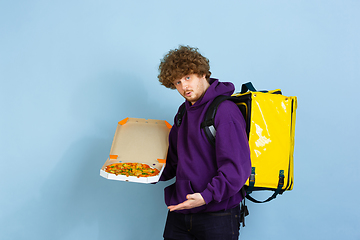 Image showing Contacless delivery service during quarantine. Man delivers food and shopping bags during insulation. Emotions of deliveryman isolated on blue background.