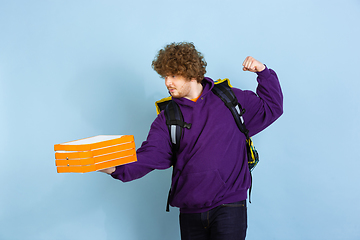 Image showing Contacless delivery service during quarantine. Man delivers food and shopping bags during insulation. Emotions of deliveryman isolated on blue background.