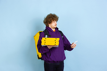 Image showing Contacless delivery service during quarantine. Man delivers food and shopping bags during insulation. Emotions of deliveryman isolated on blue background.