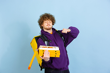 Image showing Contacless delivery service during quarantine. Man delivers food and shopping bags during insulation. Emotions of deliveryman isolated on blue background.